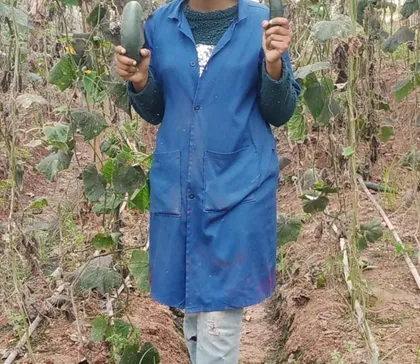 Cynthia in a work coat holding two freshly picked courgettes in a vegetable field