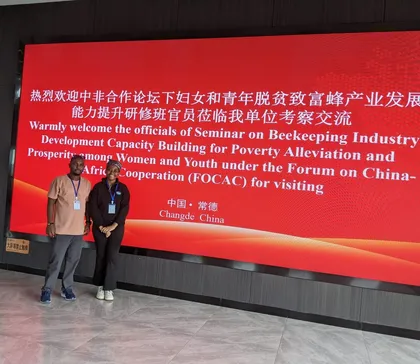 Two team members in front of the FOCAC beekeeping seminar welcome screen in Changde, China